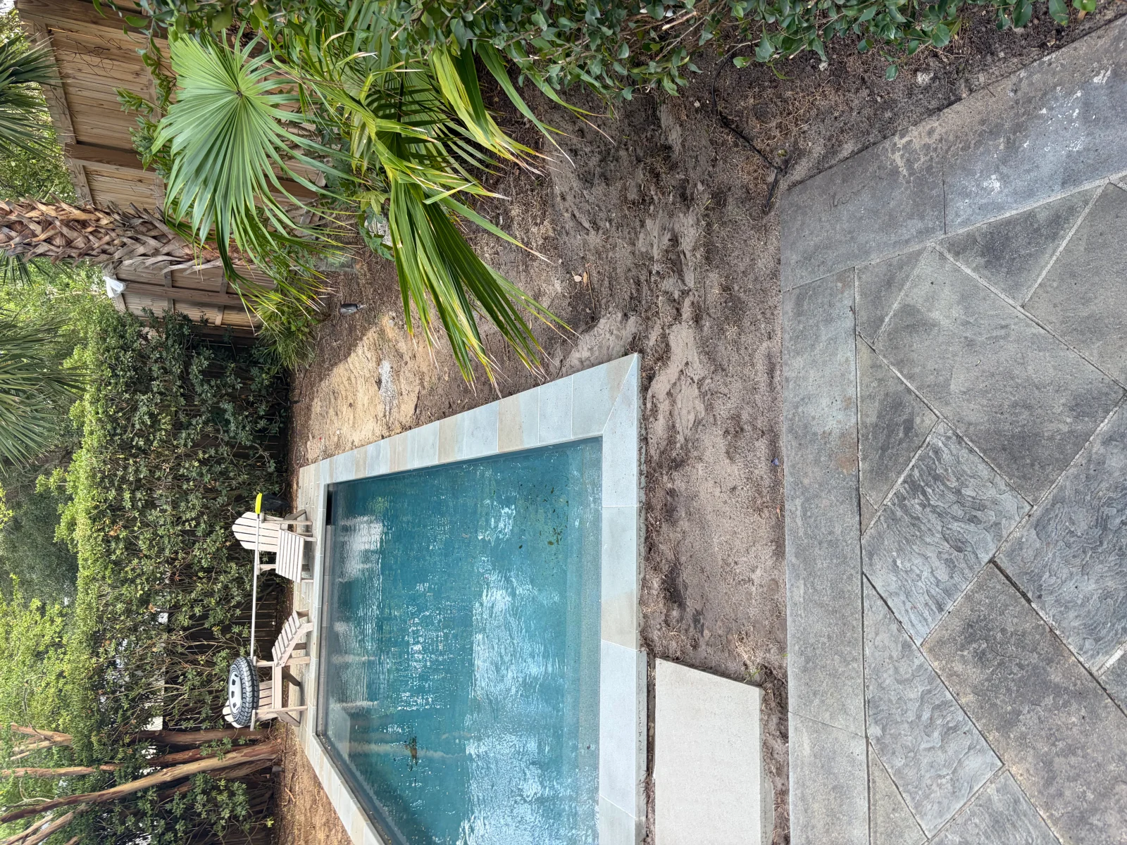 Gray herringbone porcelain pavers around in-ground pool with white coping and tropical plants