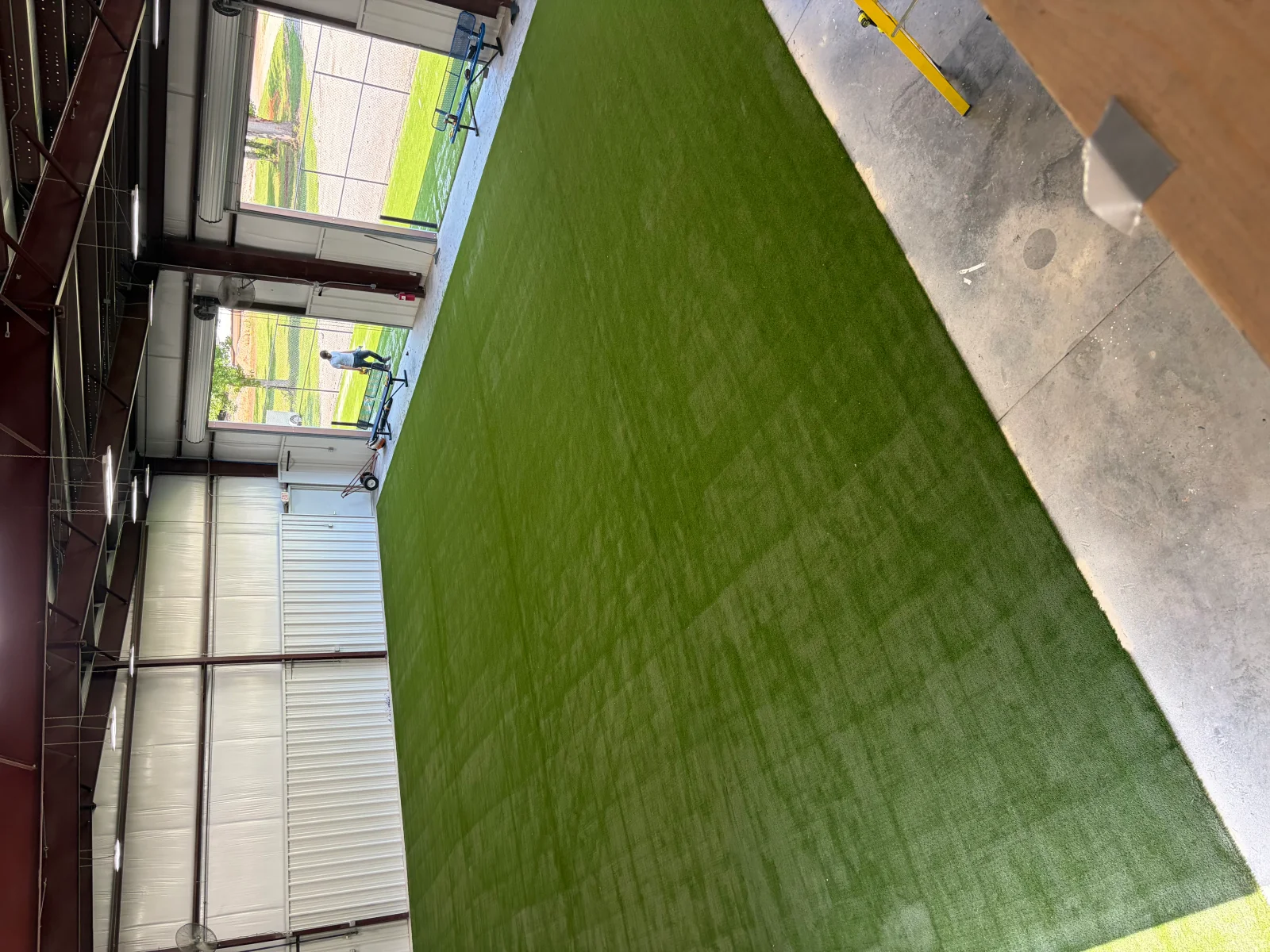 Indoor golf facility with synthetic green turf, concrete borders, and overhead lighting system