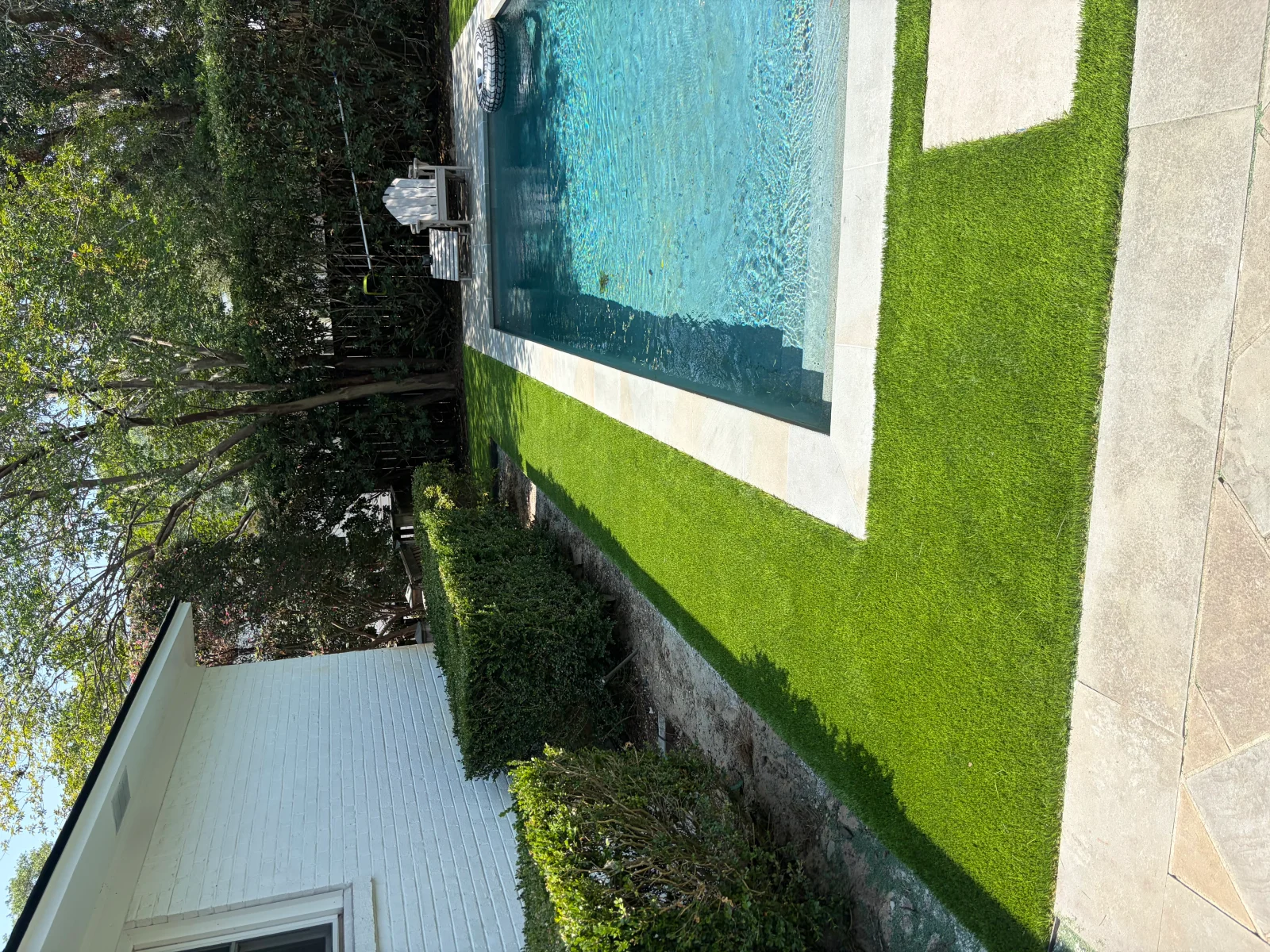 Installed turf grass lawn with concrete patio, mature landscaping, and established trees