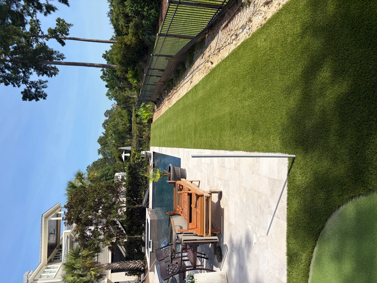 Residential backyard with installed putting green, mature landscaping, and pergola structure