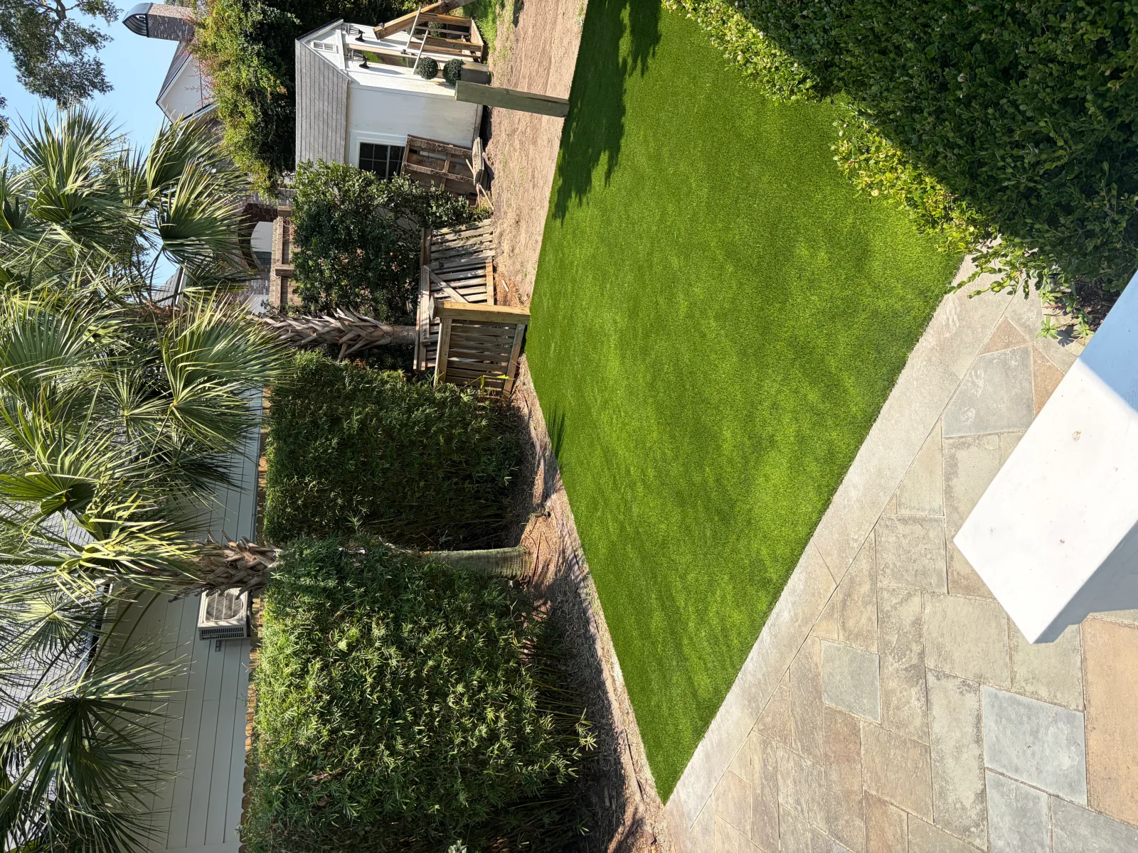 Manicured residential lawn with stone patio, hedges, and palm landscaping